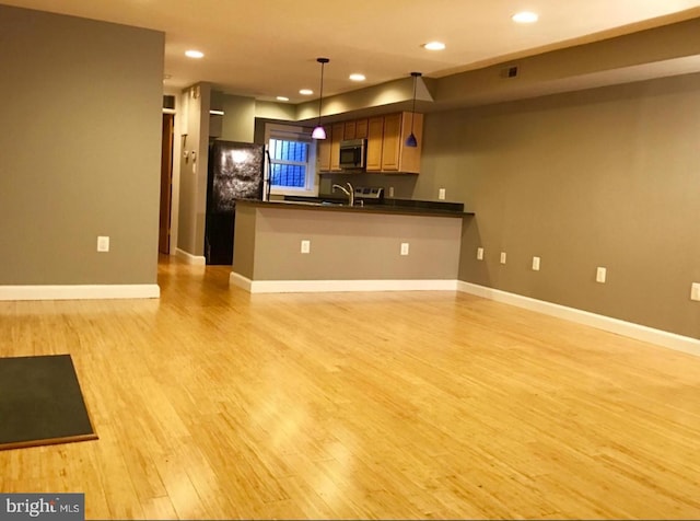 kitchen featuring freestanding refrigerator, a peninsula, dark countertops, light wood-style floors, and stainless steel microwave