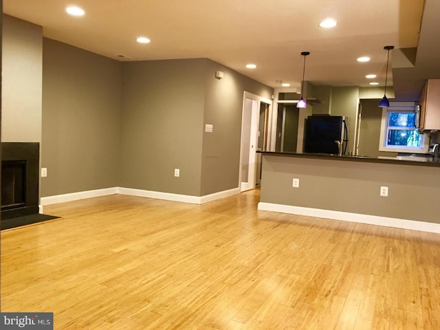 unfurnished living room featuring recessed lighting, a fireplace with flush hearth, light wood-style flooring, and baseboards