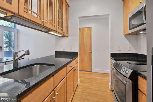 kitchen featuring brown cabinets, a sink, light wood finished floors, dark stone counters, and stainless steel appliances