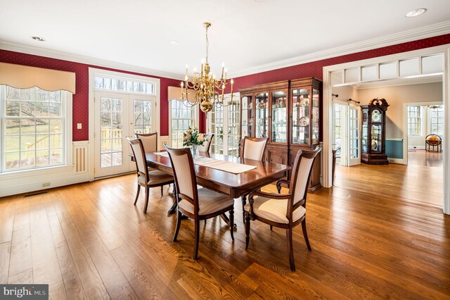 dining space with wood-type flooring, french doors, an inviting chandelier, and ornamental molding