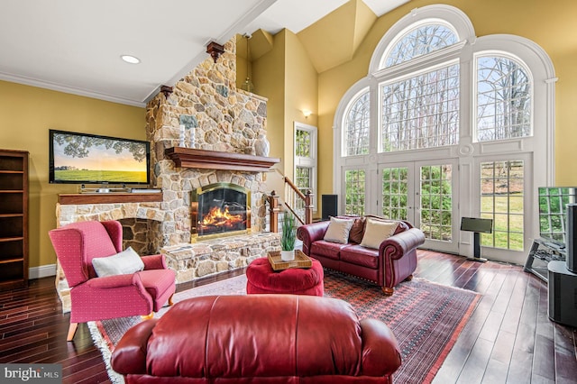 living room featuring crown molding, a towering ceiling, a stone fireplace, and hardwood / wood-style flooring