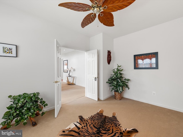 living area featuring light colored carpet, baseboards, and ceiling fan
