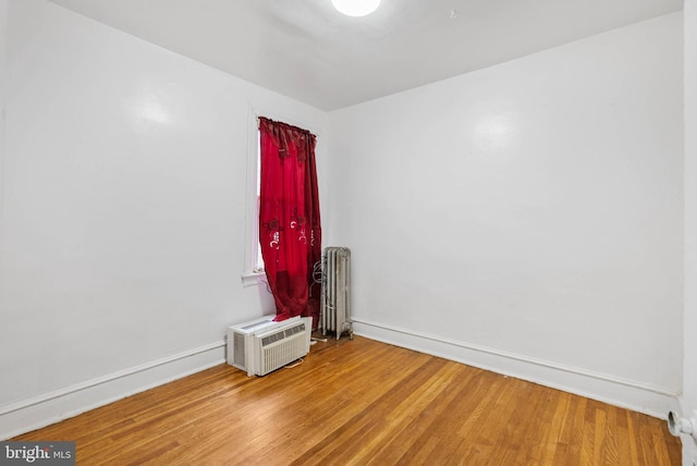 unfurnished room featuring wood finished floors, radiator heating unit, baseboards, and an AC wall unit