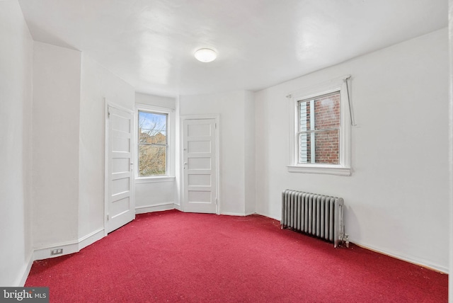 spare room with dark carpet, radiator heating unit, and baseboards