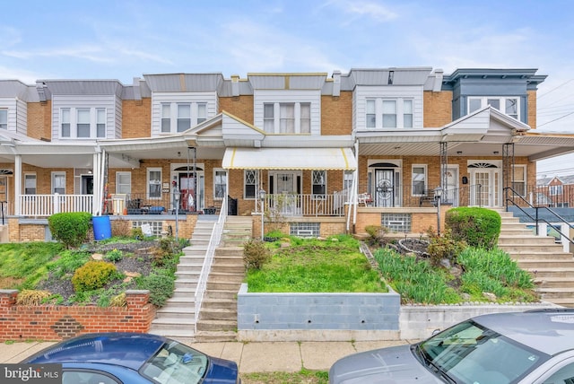 multi unit property featuring stairway, brick siding, and covered porch