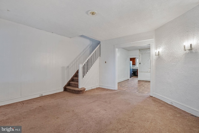 interior space featuring a textured wall, baseboards, stairway, and carpet floors