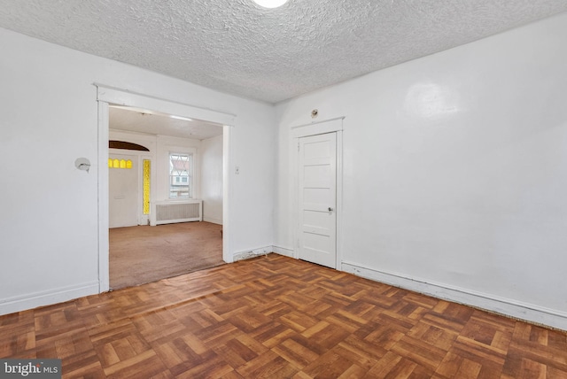 empty room with radiator heating unit, arched walkways, baseboards, and a textured ceiling