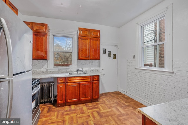 kitchen with radiator, appliances with stainless steel finishes, light countertops, a sink, and brick wall