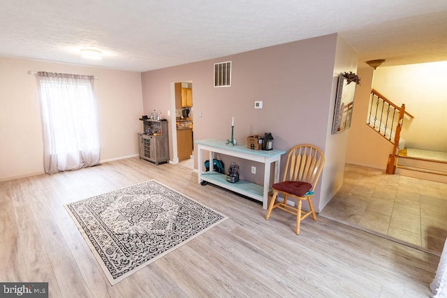 sitting room with light wood-style floors, a textured ceiling, visible vents, stairway, and baseboards