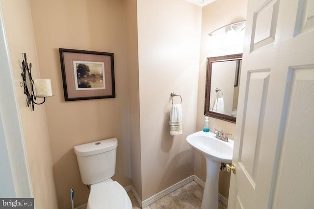 half bathroom with a sink, toilet, and baseboards