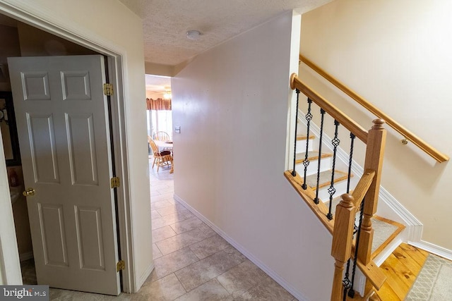 corridor with stairway, a textured ceiling, baseboards, and light tile patterned floors