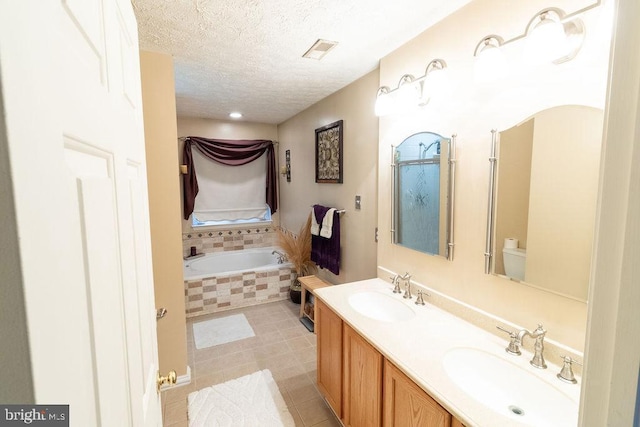 full bathroom with visible vents, a textured ceiling, a sink, and tiled bath