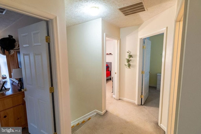 hall featuring visible vents, baseboards, light colored carpet, and a textured ceiling