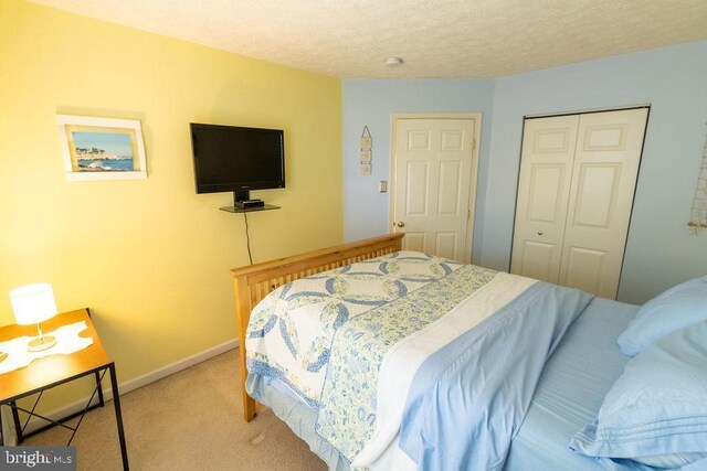 bedroom with light carpet, baseboards, a textured ceiling, and a closet