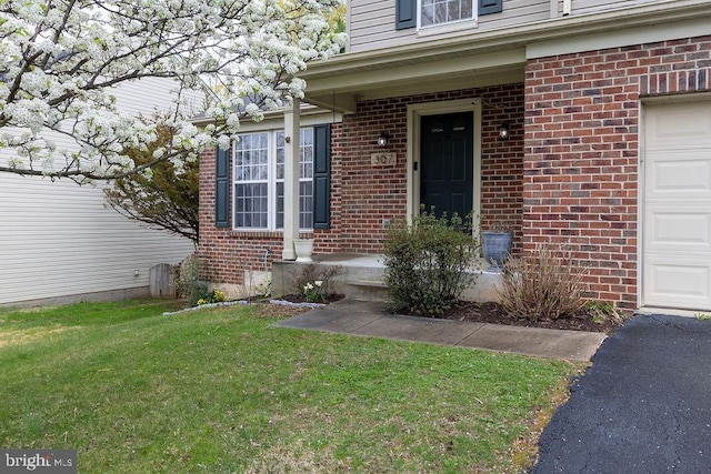 entrance to property with brick siding, a yard, and a garage
