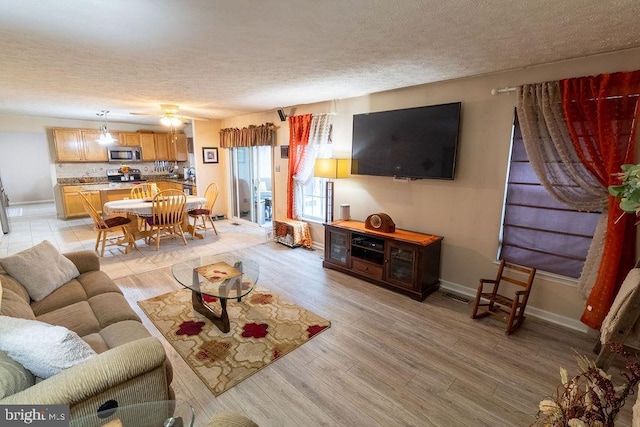 living room featuring ceiling fan, light wood-type flooring, a textured ceiling, visible vents, and baseboards