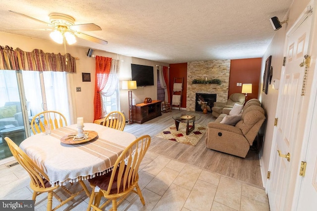 dining area with light tile patterned floors, visible vents, a stone fireplace, a ceiling fan, and a textured ceiling