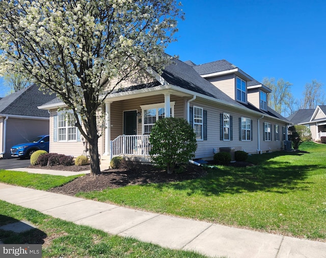 cape cod home with a porch, roof with shingles, a front yard, and central AC unit
