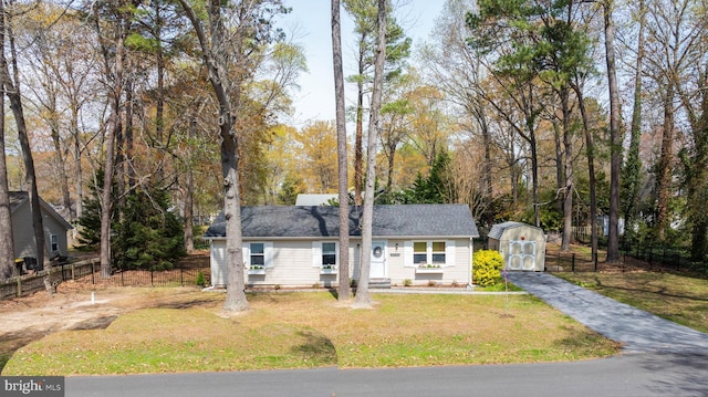 view of front facade featuring a storage shed, a front lawn, fence, and an outbuilding
