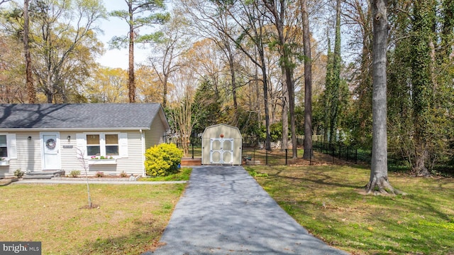 view of front of property with aphalt driveway, an outdoor structure, fence, a storage unit, and a front lawn
