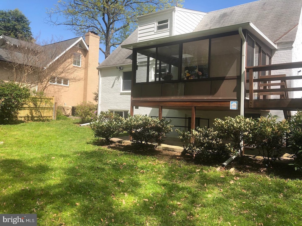 rear view of property featuring a sunroom, a lawn, roof with shingles, and brick siding