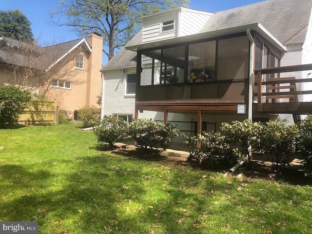 rear view of property featuring a sunroom, a lawn, roof with shingles, and brick siding