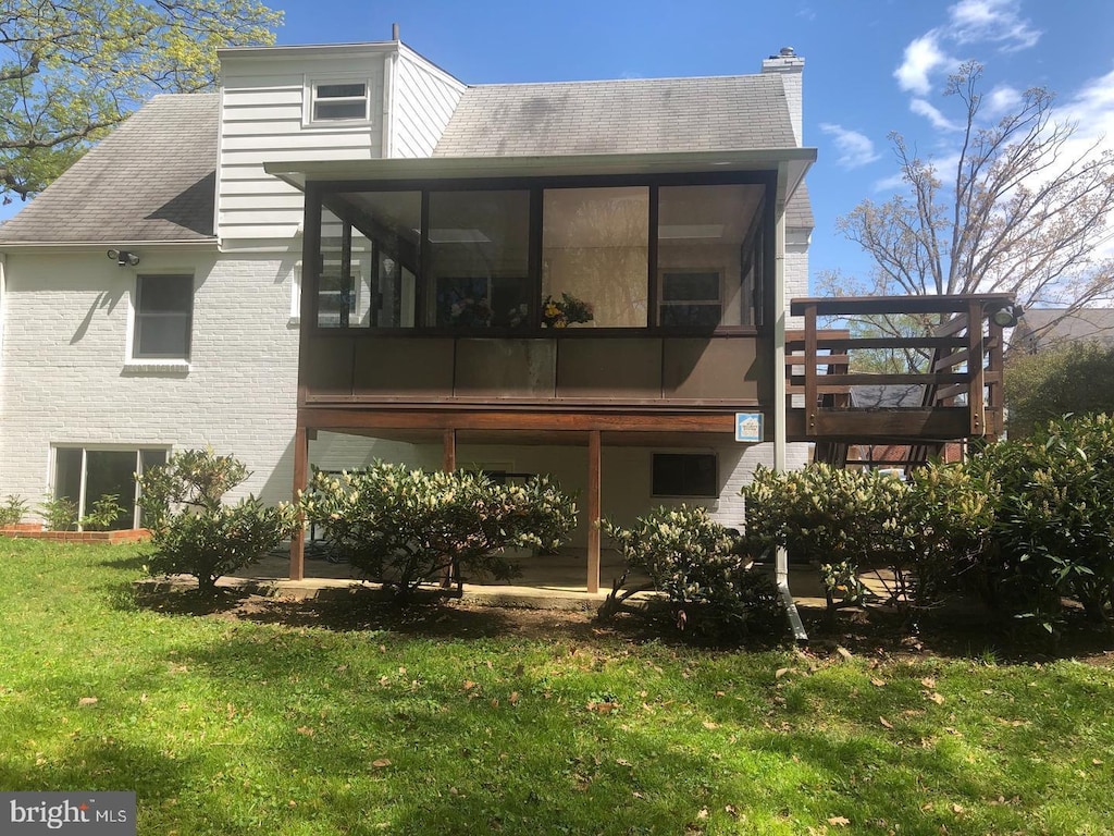 back of property featuring a yard, a chimney, a sunroom, and brick siding