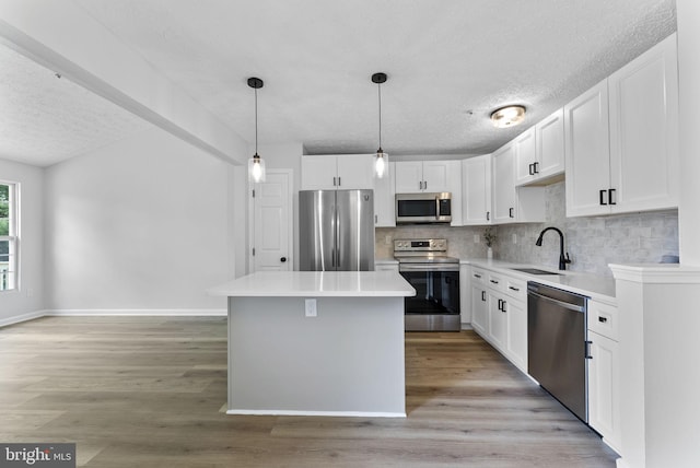kitchen with a textured ceiling, a center island, appliances with stainless steel finishes, a sink, and decorative backsplash