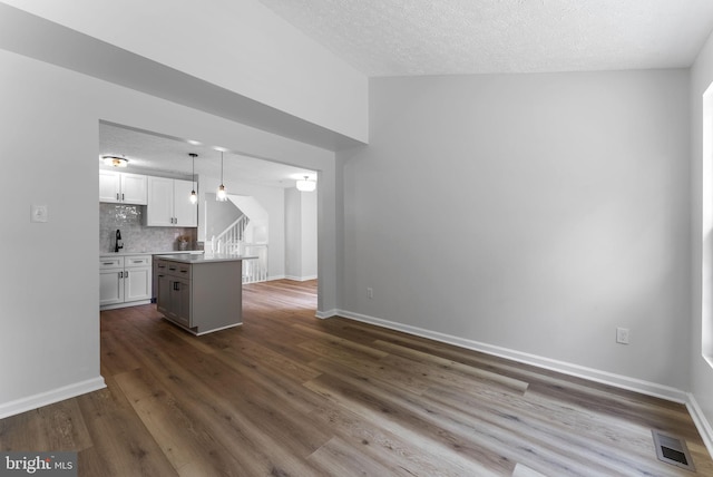 unfurnished living room featuring visible vents, baseboards, a textured ceiling, stairway, and dark wood-type flooring