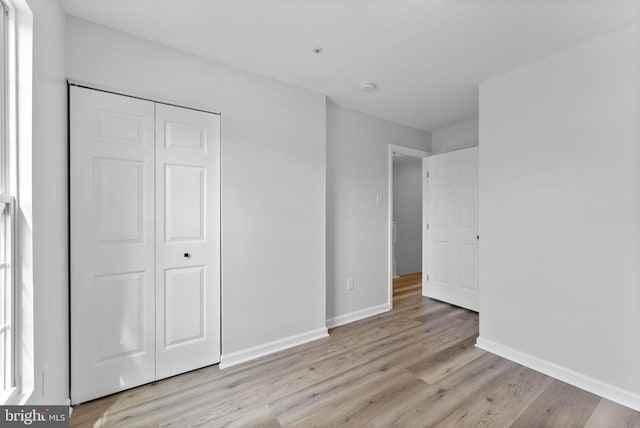 unfurnished bedroom with a closet, light wood finished floors, and baseboards