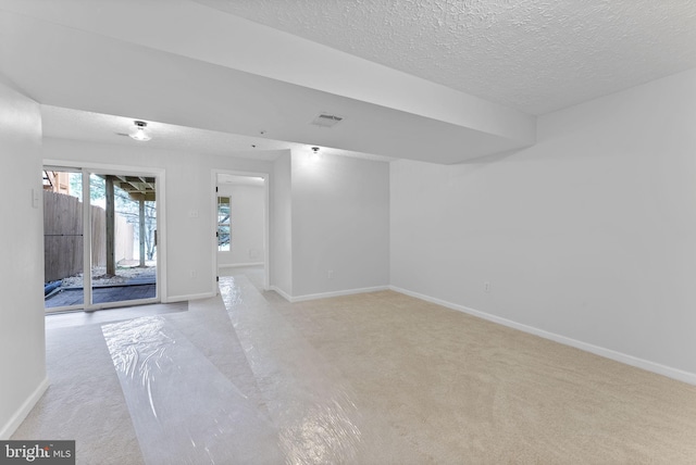 unfurnished room featuring a textured ceiling, light colored carpet, baseboards, and visible vents