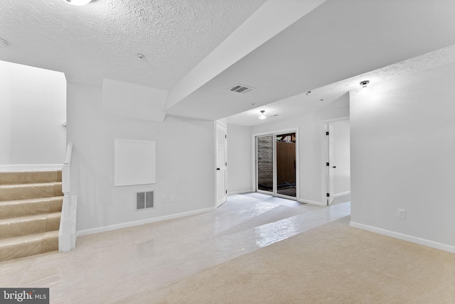 unfurnished room featuring a textured ceiling, light colored carpet, visible vents, and stairs