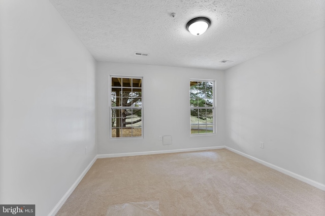 carpeted empty room featuring a textured ceiling, baseboards, and visible vents