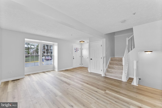 unfurnished living room with stairs, light wood finished floors, a textured ceiling, and baseboards