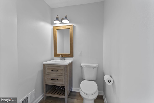 half bathroom featuring visible vents, toilet, vanity, and wood finished floors