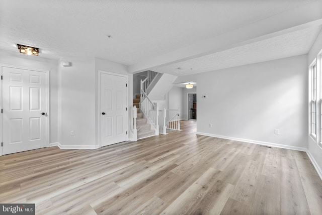 unfurnished living room featuring stairway, baseboards, and light wood-type flooring