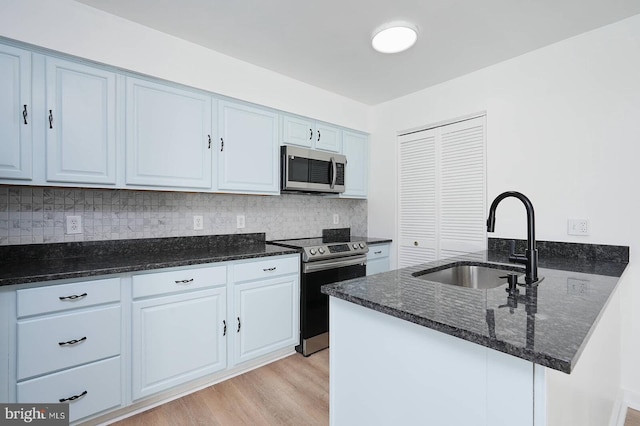 kitchen featuring light wood finished floors, dark stone countertops, a sink, a peninsula, and appliances with stainless steel finishes