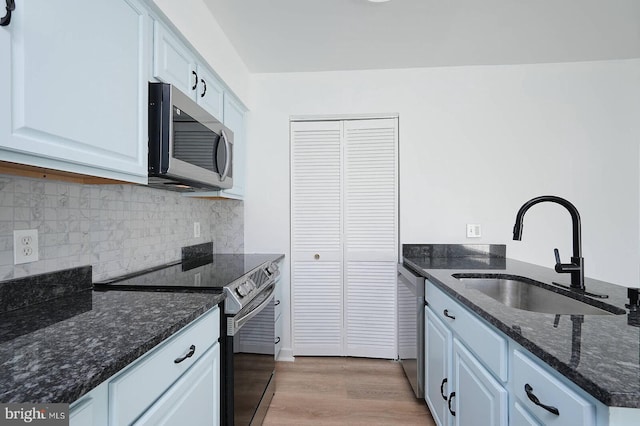 kitchen featuring light wood finished floors, a sink, dark stone countertops, decorative backsplash, and appliances with stainless steel finishes