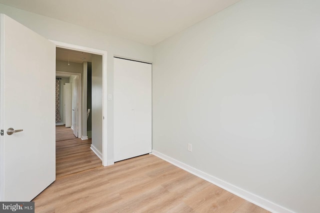unfurnished bedroom with light wood-style flooring, baseboards, and a closet