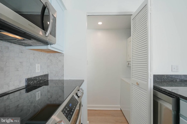 kitchen featuring tasteful backsplash, dark stone countertops, light wood finished floors, stainless steel microwave, and white cabinetry