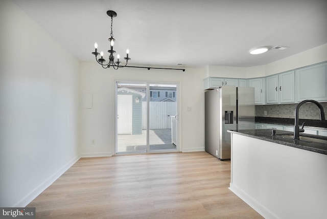 kitchen featuring a sink, dark stone counters, a chandelier, stainless steel fridge, and light wood-style flooring