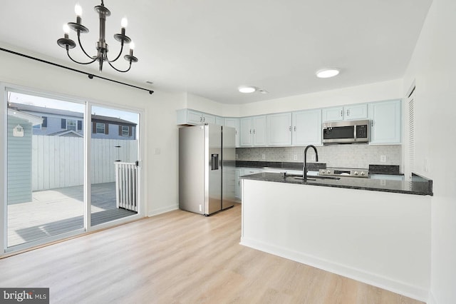 kitchen featuring stainless steel appliances, dark stone counters, light wood-type flooring, an inviting chandelier, and decorative backsplash