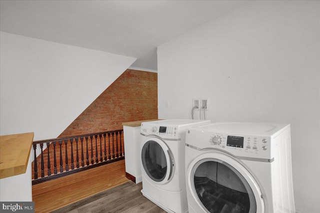 washroom featuring brick wall, washer and clothes dryer, wood finished floors, and laundry area