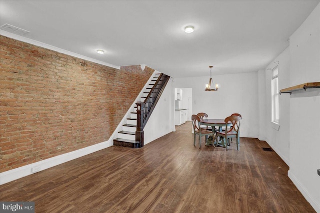 unfurnished dining area with visible vents, wood finished floors, stairs, brick wall, and a notable chandelier