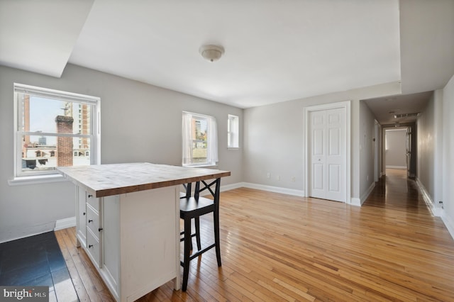 kitchen featuring light wood-type flooring, white cabinets, butcher block countertops, a breakfast bar area, and baseboards