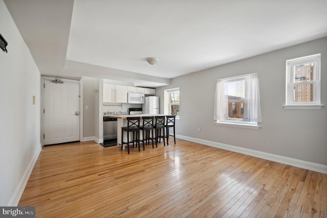 kitchen featuring baseboards, white appliances, white cabinetry, light wood-style floors, and a breakfast bar area