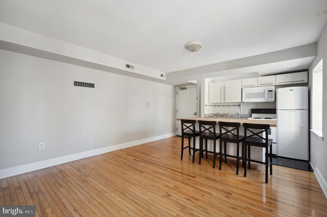 kitchen featuring white appliances, a kitchen bar, light wood-style flooring, white cabinets, and baseboards