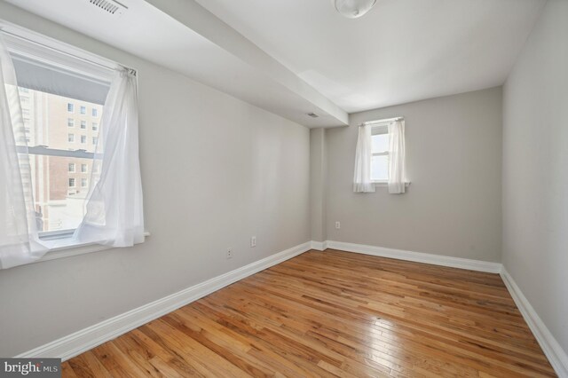spare room featuring wood-type flooring, visible vents, and baseboards