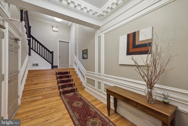 entryway with visible vents, a decorative wall, crown molding, wood finished floors, and stairs