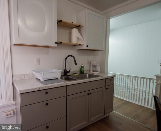kitchen featuring dark wood-type flooring, open shelves, gray cabinets, light stone counters, and a sink